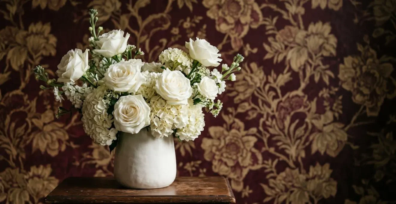 Elegant monochromatic white floral arrangement positioned against boldly patterned living room wallpaper creating visual harmony