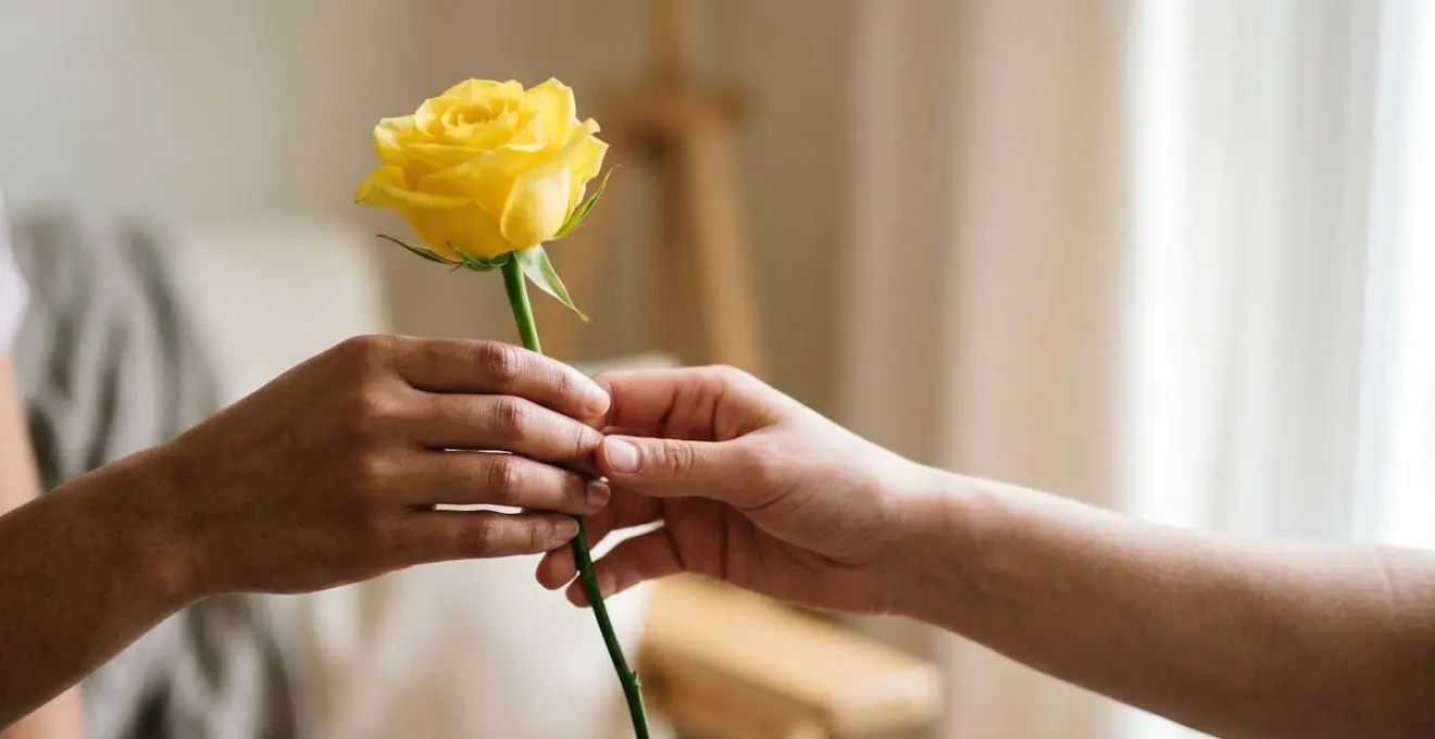 Two hands exchanging a single yellow rose in warm natural light showing the contemporary gesture of platonic friendship
